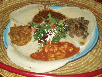 A mosob plate featuring several meats, a vegetable medley, and a mesculun mix salad with injera bread.
 