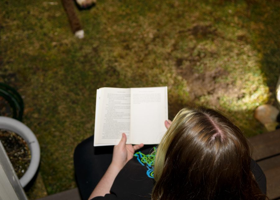 A student sits outside at night reading a book.