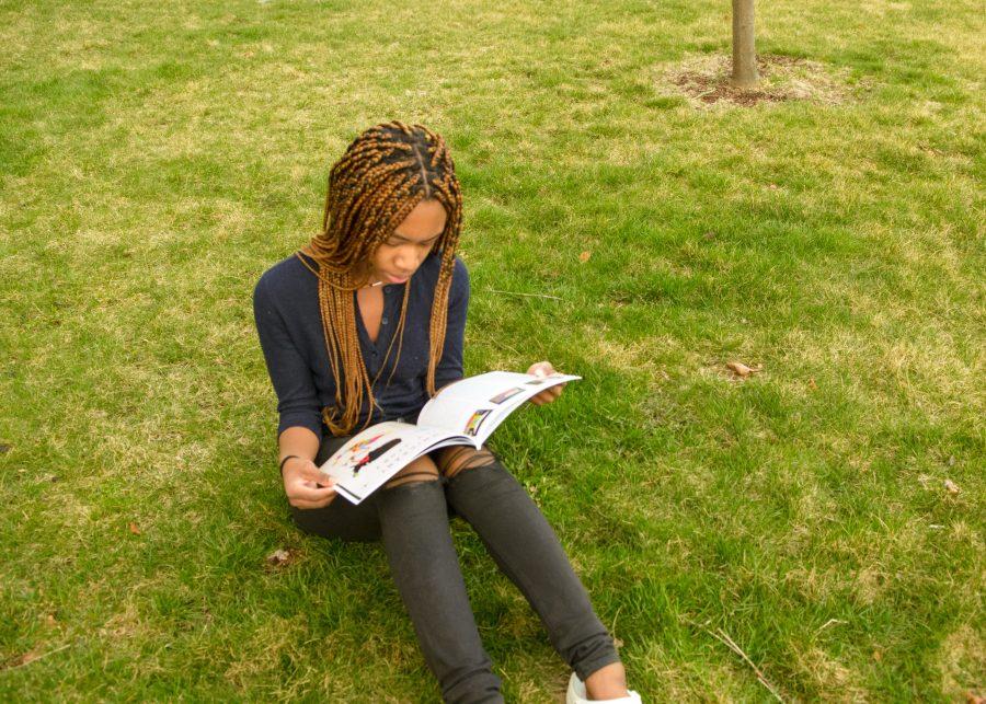 A UMass Boston student sits in front of the residence halls reading a book.