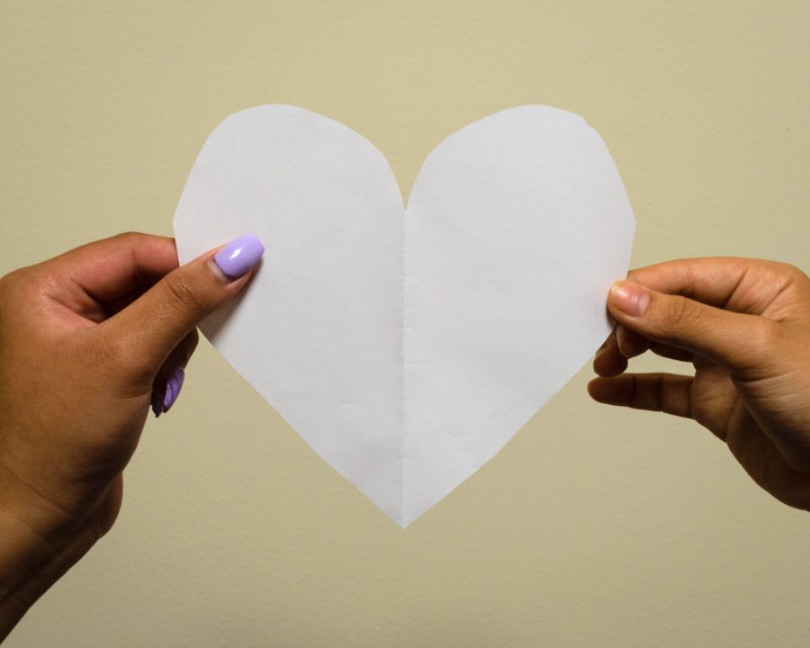 Two different hands hold a paper heart.