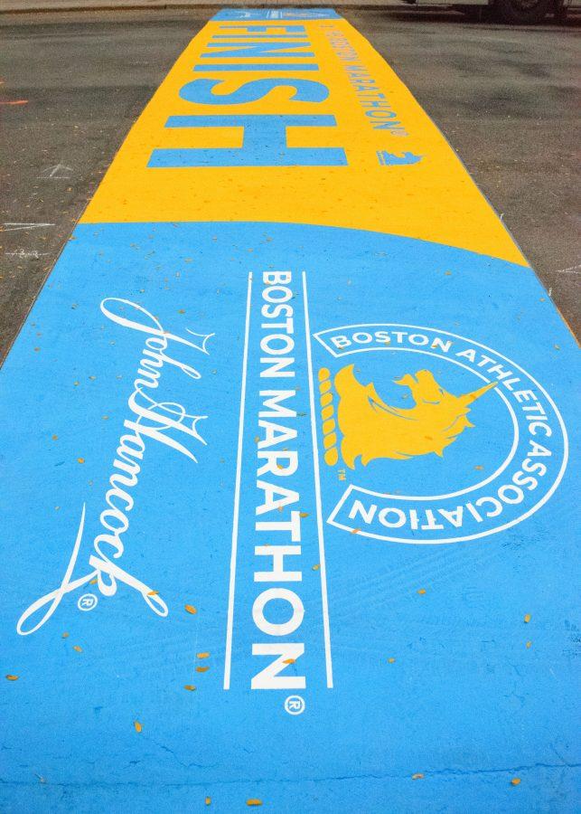 The finish line of the Boston Marathon painted on a street in Copley Square, sitting in front of Marathon Sports.