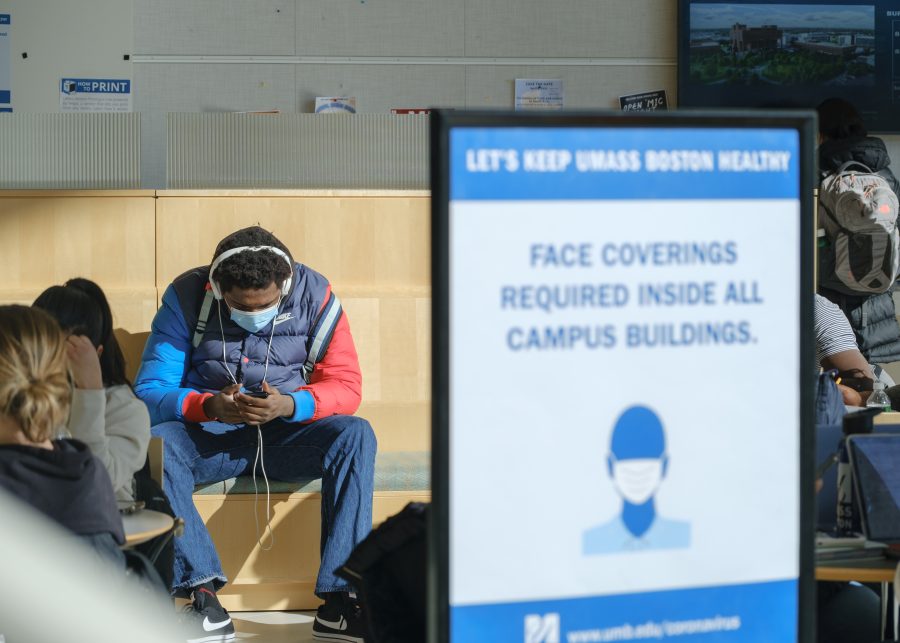 A UMass Boston student sits next to a COVID mask protocol notice in University Hall.