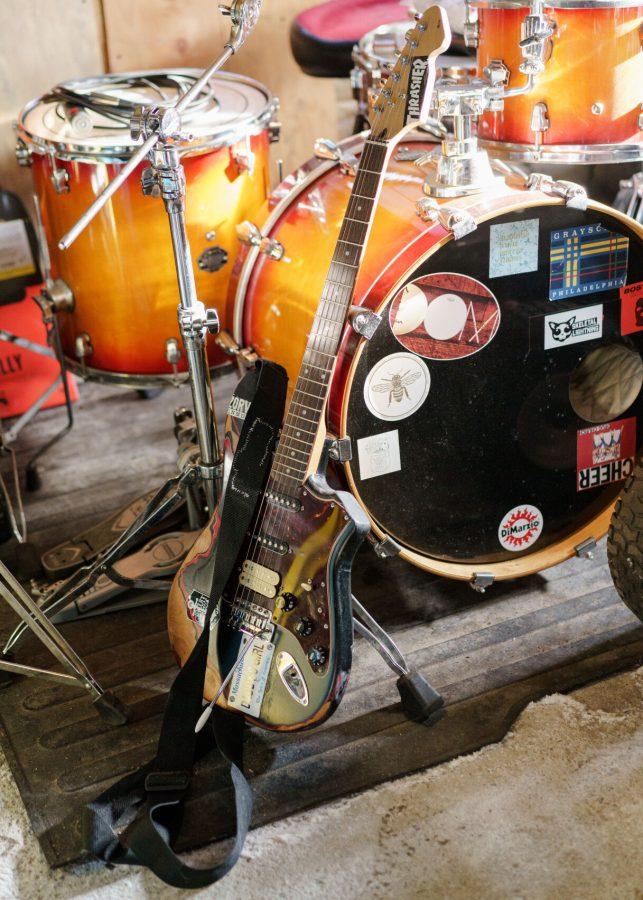 A guitar leans against the side of a drum set within a garage studio.