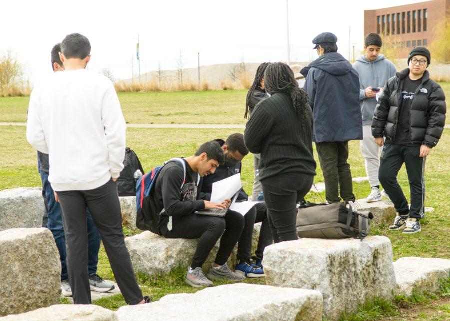UMass Boston students look over some papers on the lawn outside of campus.