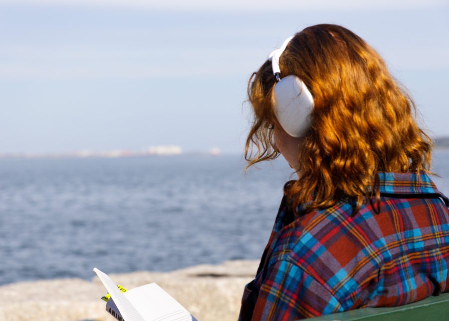 A UMass Boston student sits with a book at the Harborwalk just off campus.