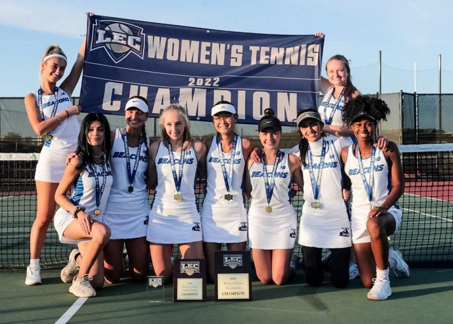 UMass Boston’s women’s tennis team holds up a championship banner.
