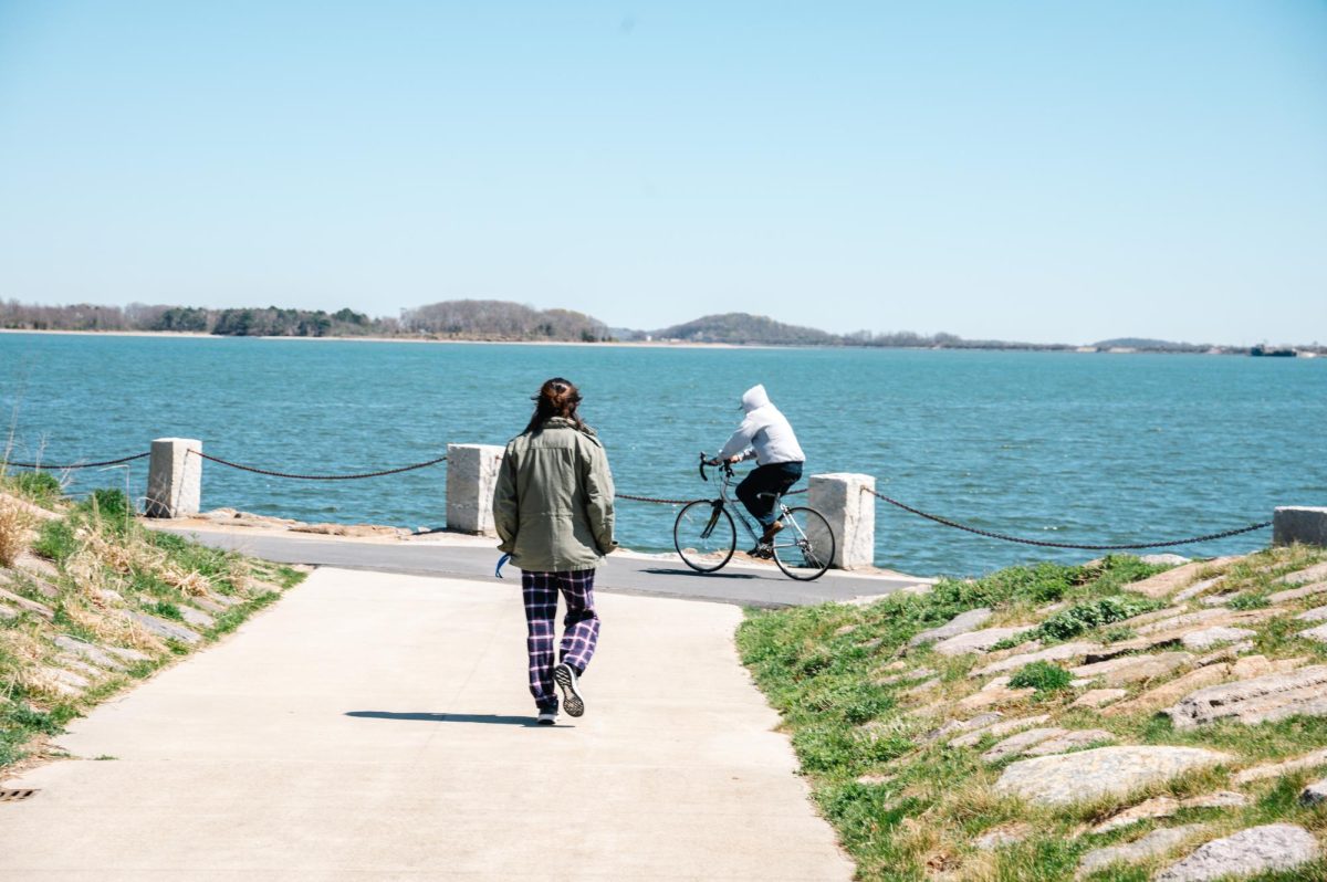 A student walks along the Harborwalk, which surrounds the UMass Boston campus. Photo by Olivia Reid / Photography Editor.