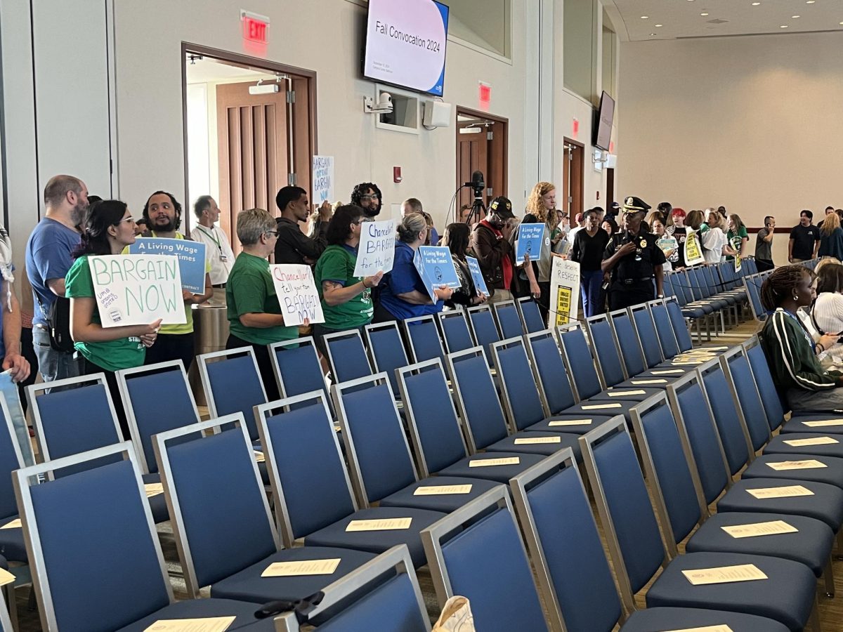 Union members and their supporters line the back of the Campus Center ballroom holding pro-union and pro-bargaining signs. 