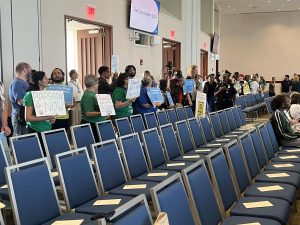 Union members and their supporters line the back of the Campus Center ballroom holding pro-union and pro-bargaining signs. 