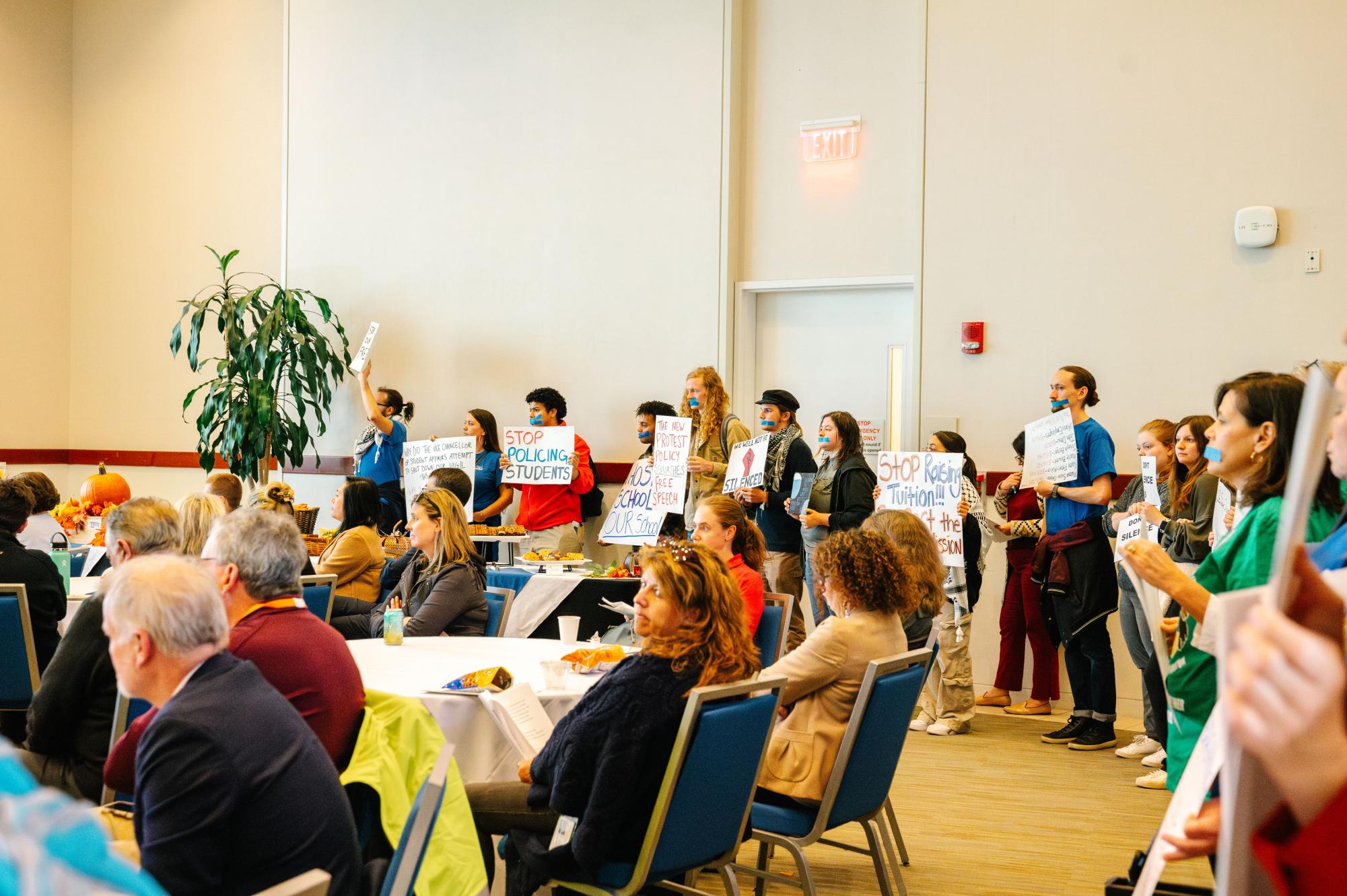 Protestors lined the back of the Campus Ballroom during the Chancellor's information session. Many had tape over their mouths and held signs demanding to be heard. 