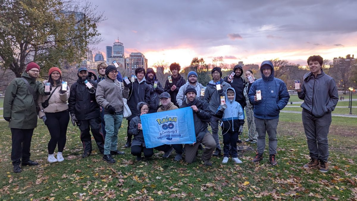 Organizers and attendees pose in front of a banner for the Pokemon Go Community Ambassador program, the group which organized the Wild Area event. 